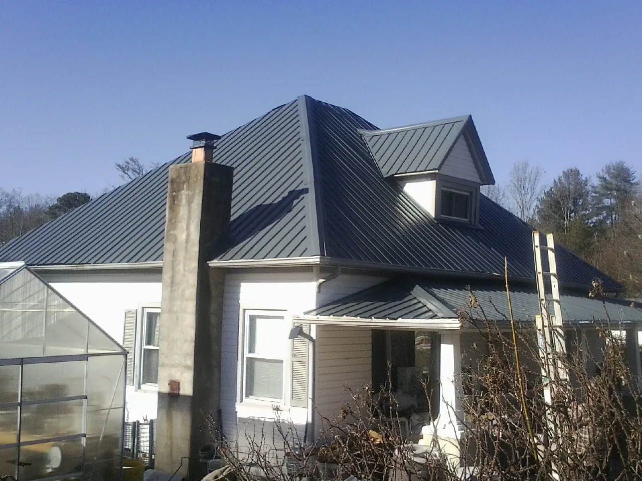 Dark blue standing seam metal roof on a white farmhouse with dormer — Slate & Tile Roof Repair by Roofing Brothers in Docena