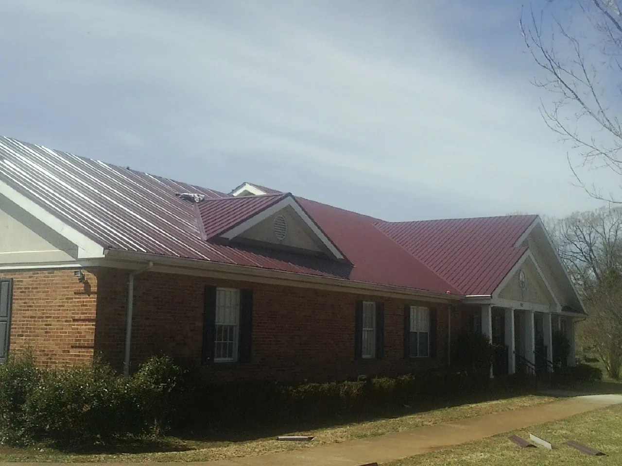 Red metal roof with gabled entries on a long brick building, from a Hail Damage Roof Repair job in Docena