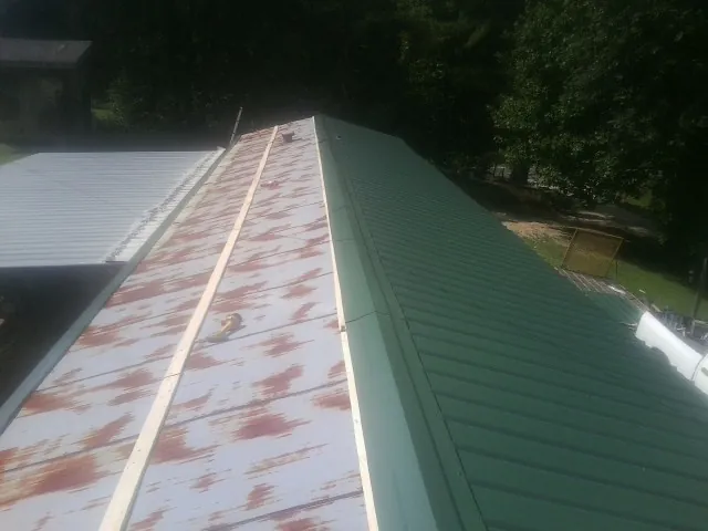 Old rusted panels beside newly installed green metal roofing — Wind Damage Roof Repair by Roofing Brothers in Docena