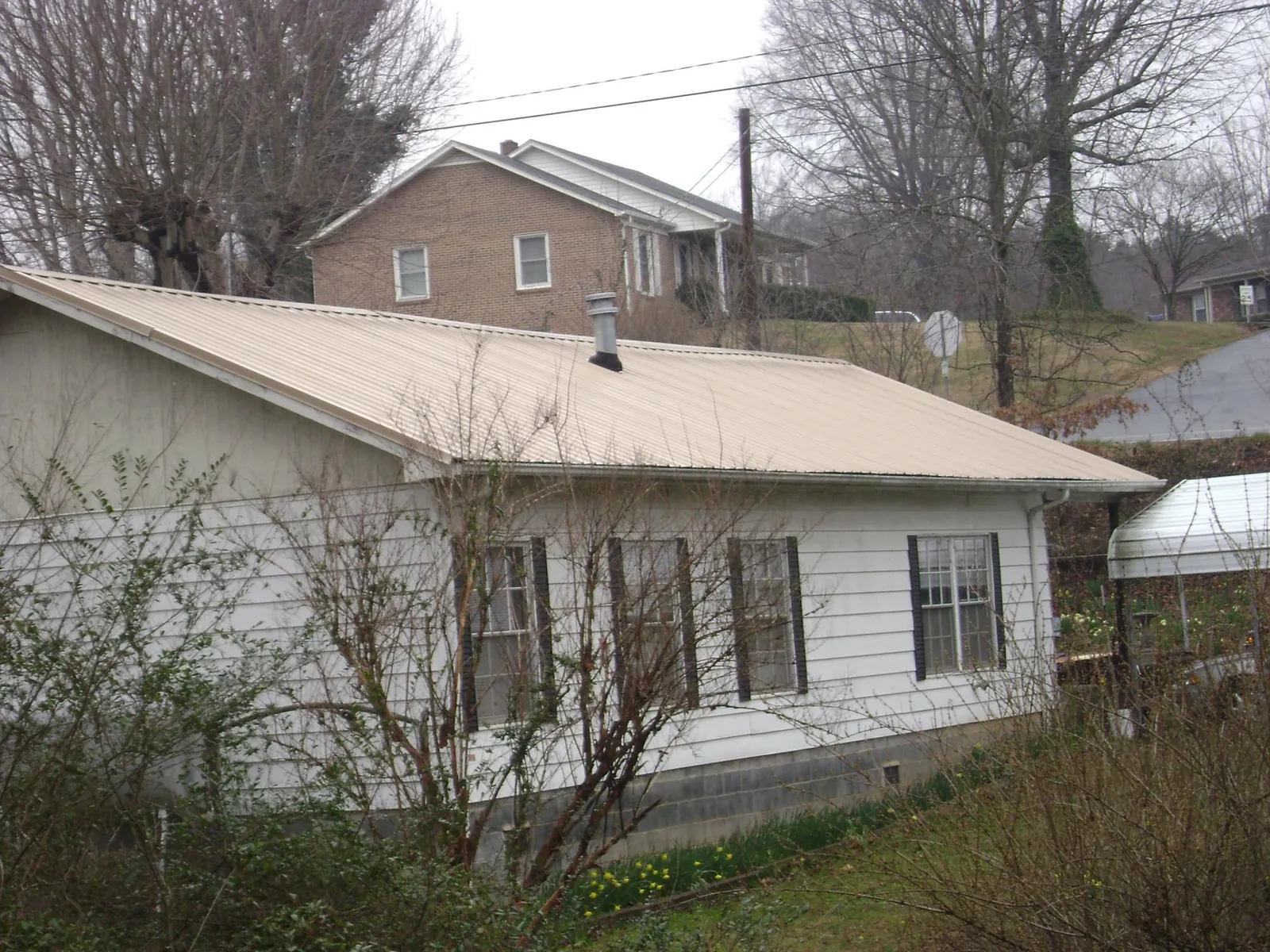Tan metal roof on a white sided house set into a hillside — Commercial Roofing by Roofing Brothers in Docena