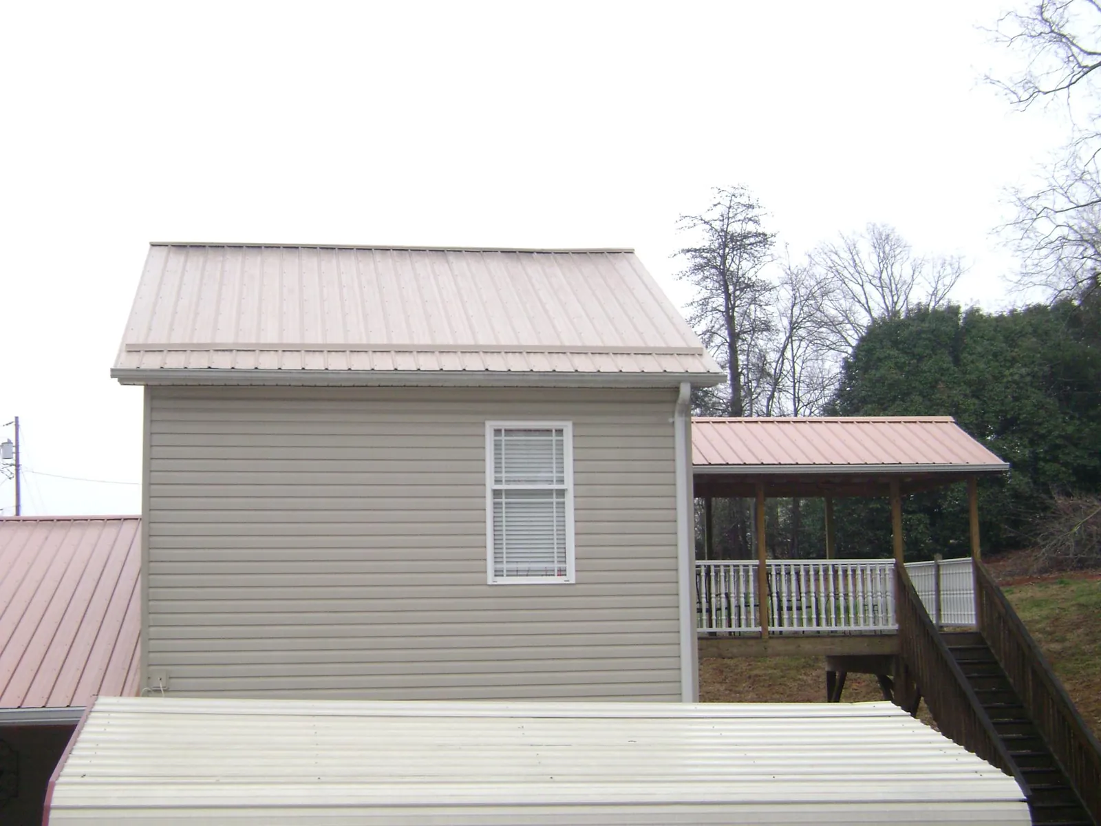 Tan metal roofs on a two story addition and attached porch, from a Roof Replacement job in Docena